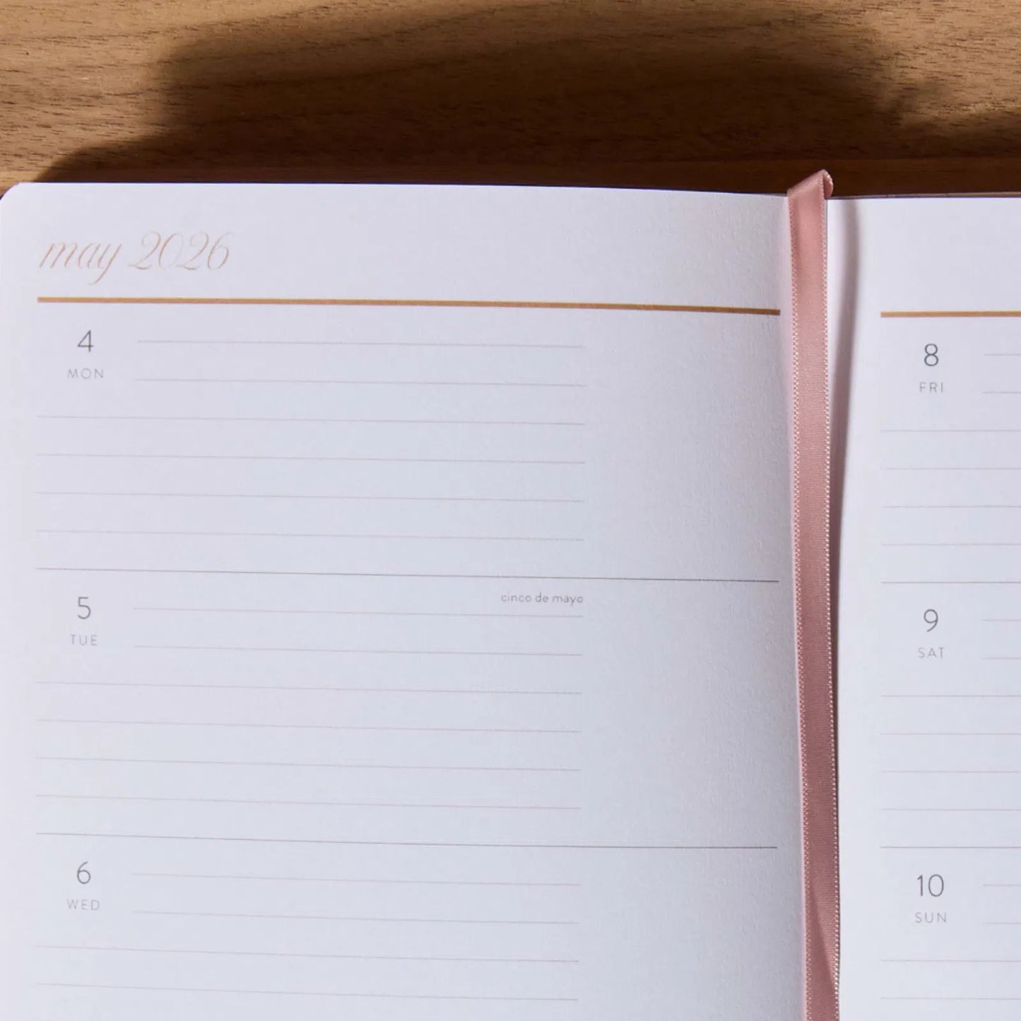 Open planner showing May 2020 with a pink ribbon bookmark on a wooden surface