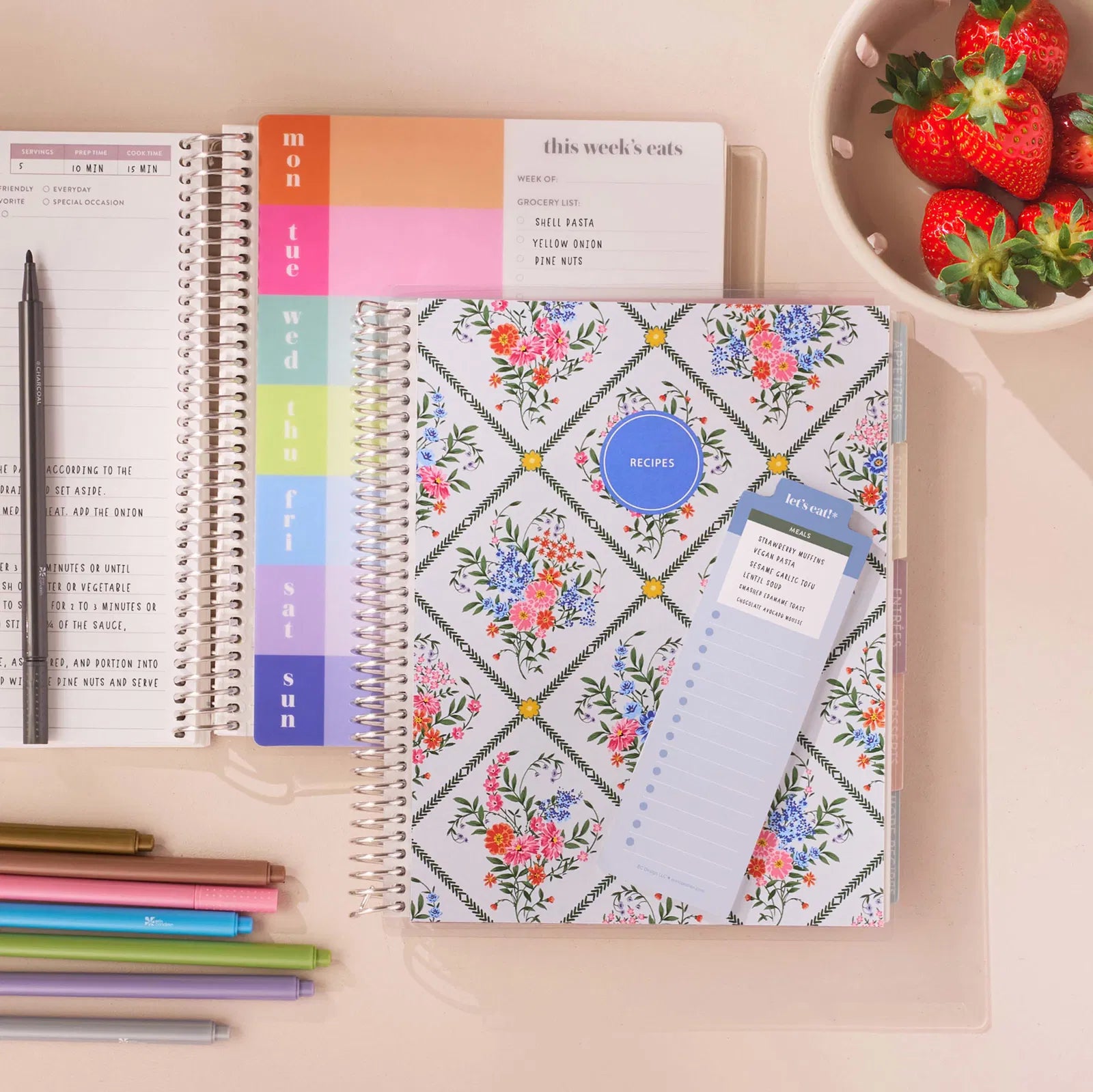 Floral planner with a weekly layout and pen on a desk with strawberries in the background