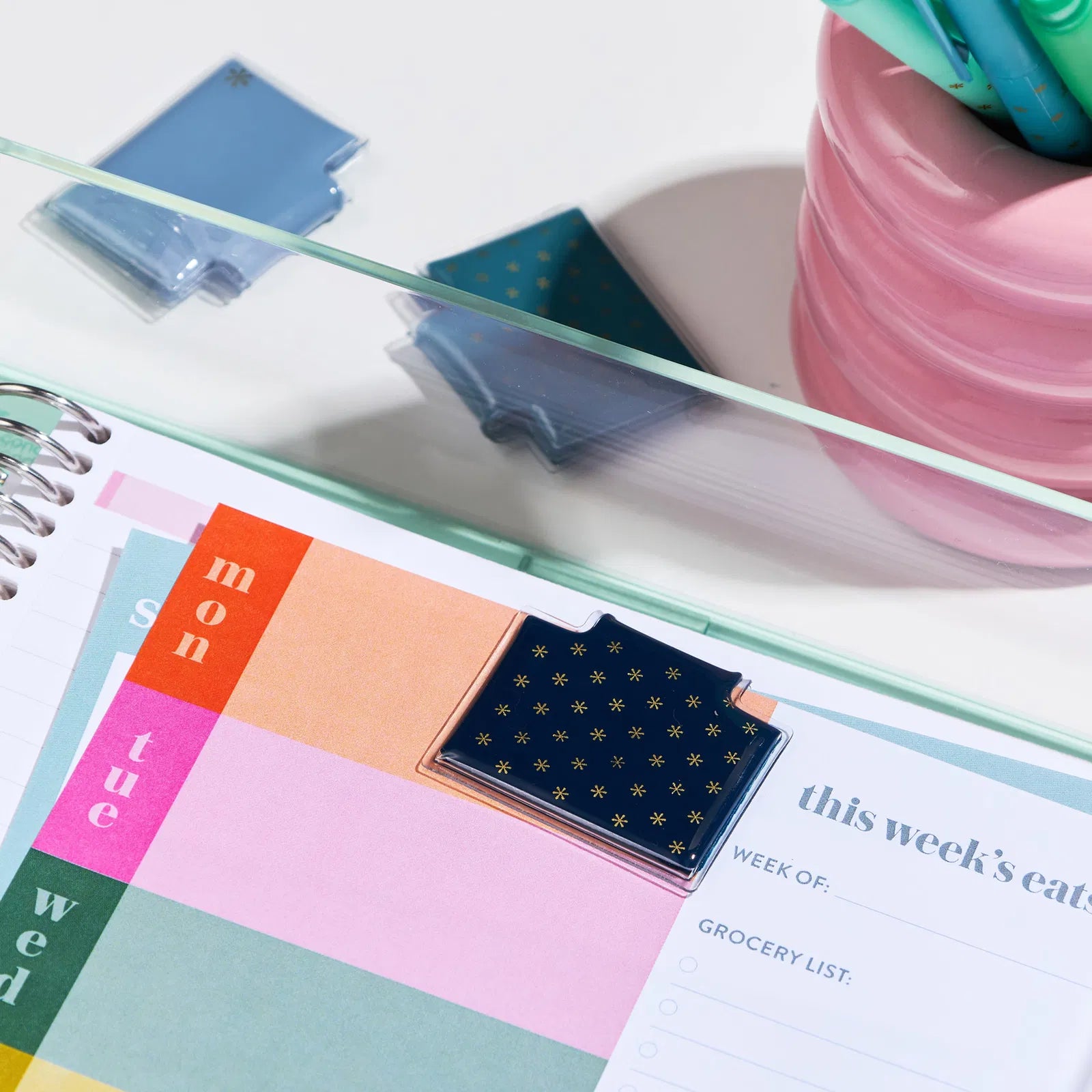 Weekly planner with colorful tabs and a pink container on a white surface
