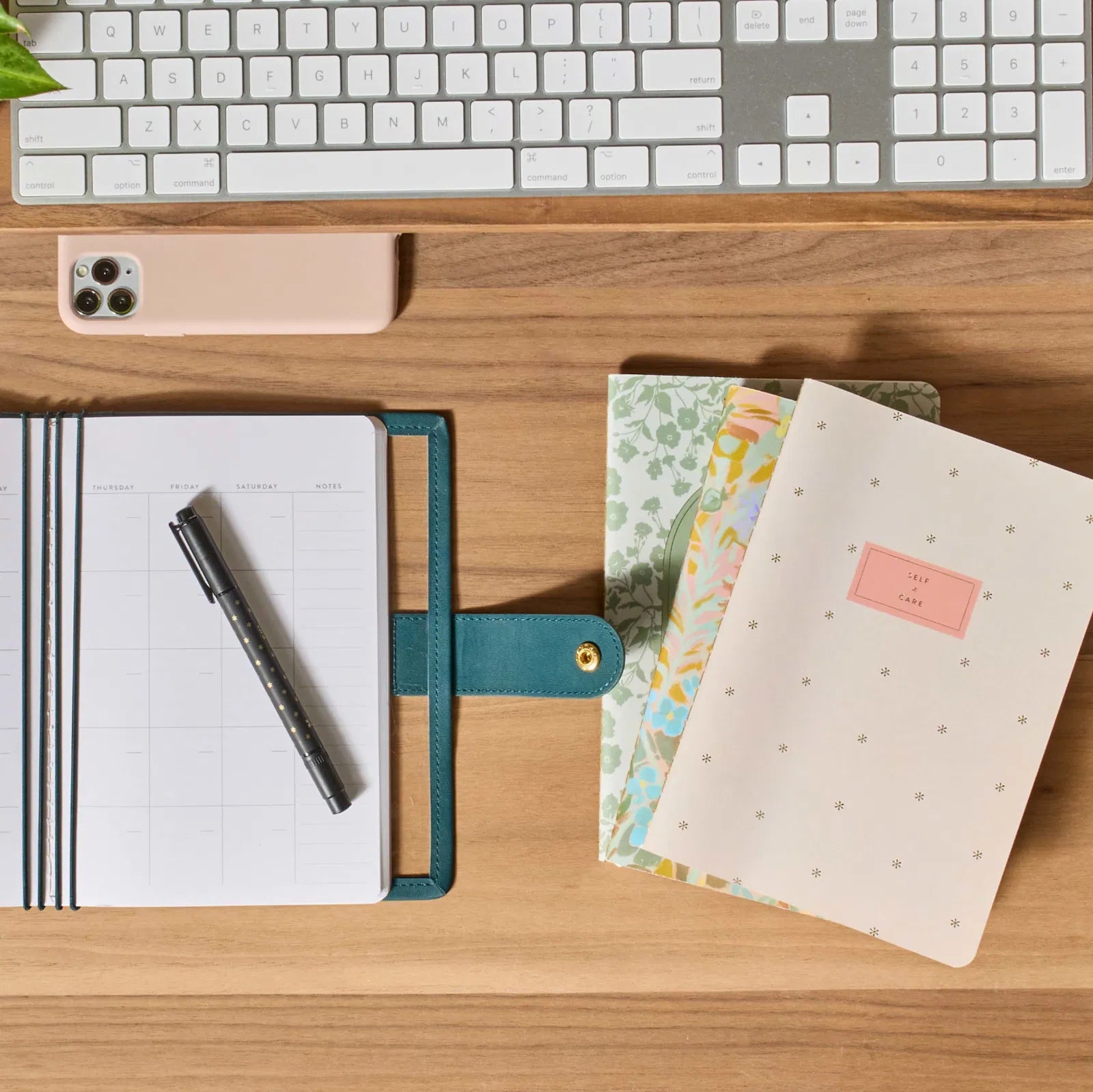 Desk setup with notebooks, pen, and keyboard on a wooden surface