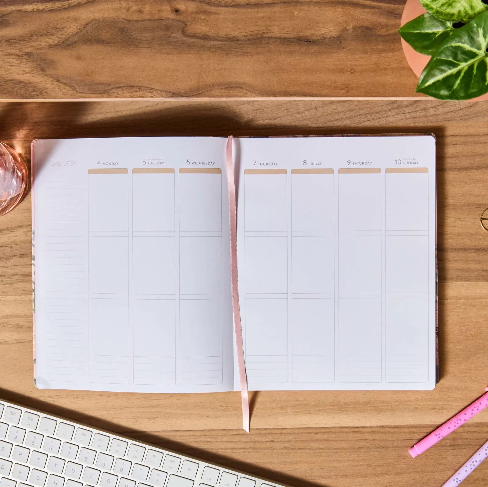 Open planner on a wooden desk with a plant and keyboard in the background