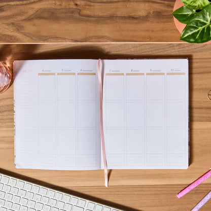 Open planner on a wooden desk with a plant and keyboard in the background