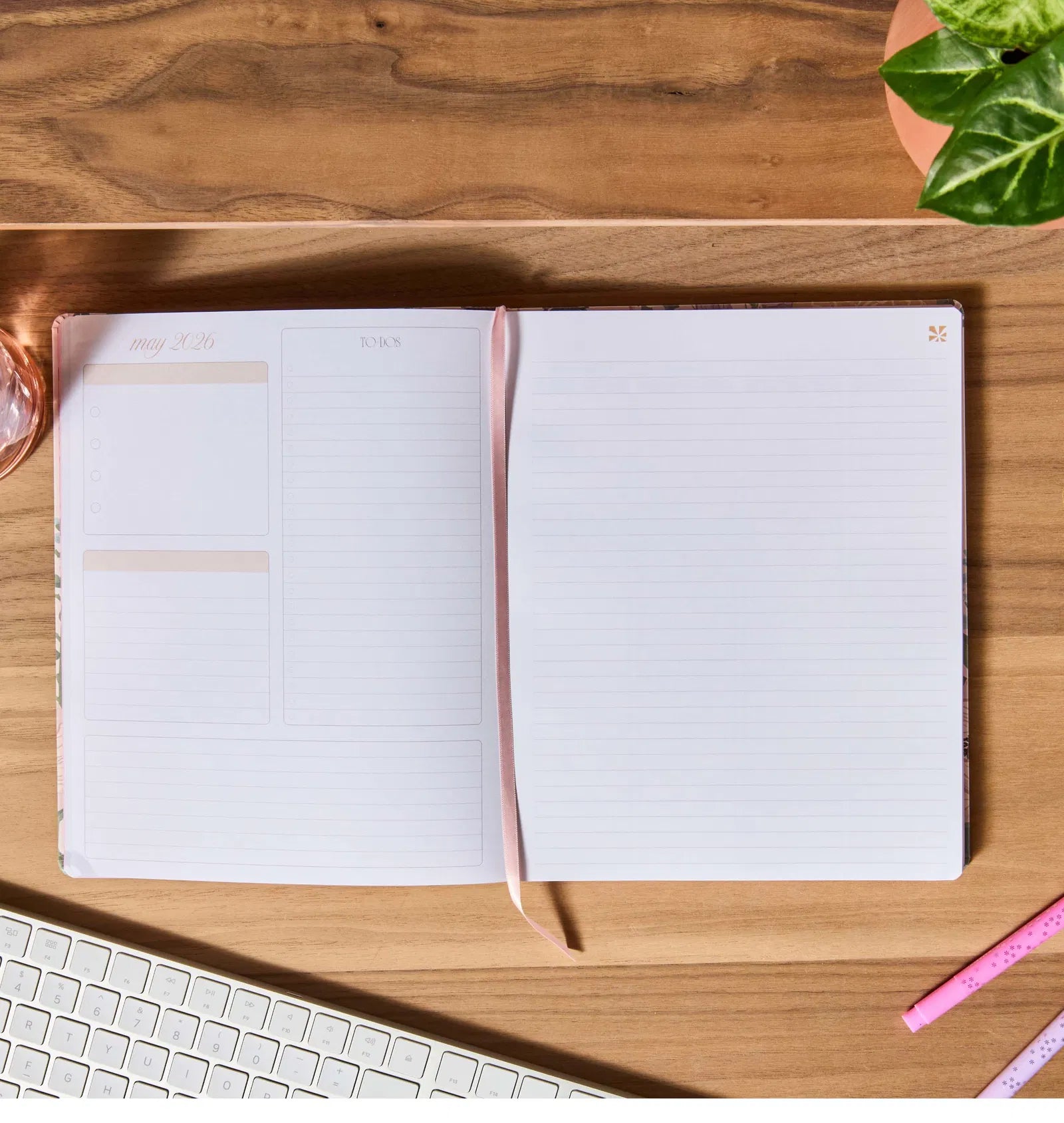 Open notebook on a wooden desk with a keyboard and plant