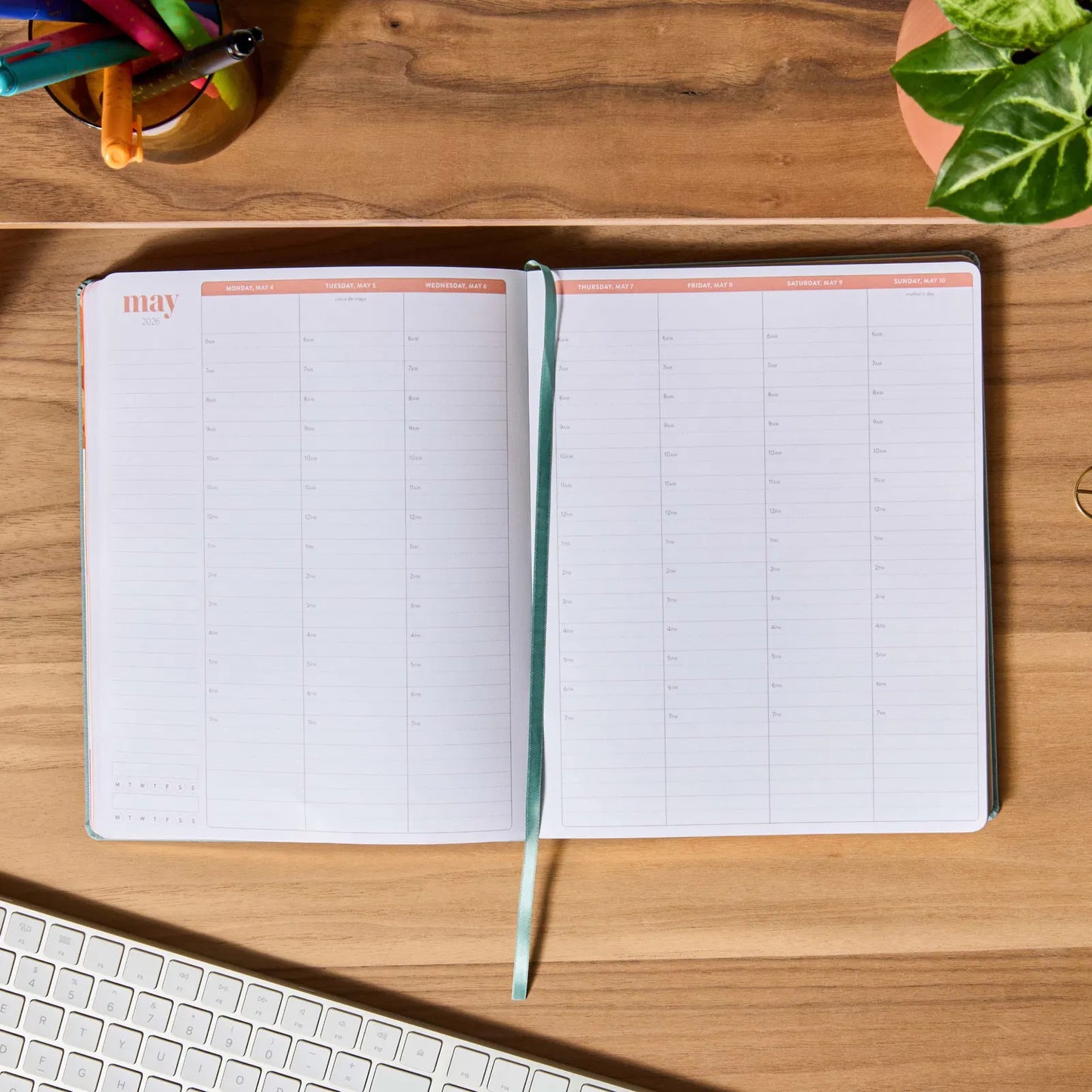 Open planner on a wooden desk with a keyboard and plant in the background