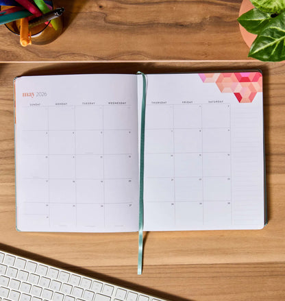 Open planner on a wooden desk with a keyboard and colorful pens.