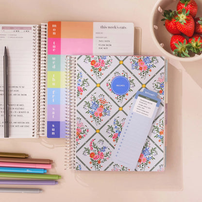 Floral planner with a weekly layout and pen on a desk with strawberries in the background