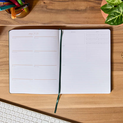 Open planner on a wooden desk with a keyboard and plant
