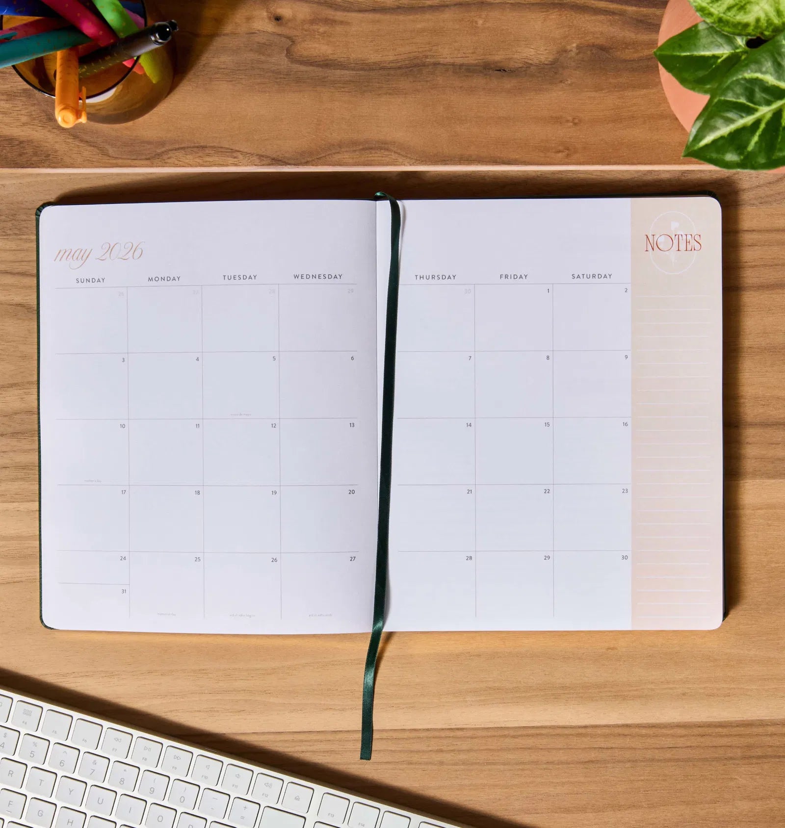 Open planner on a wooden desk with a keyboard and plant