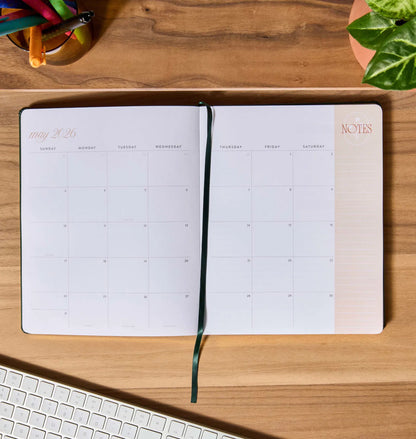 Open planner on a wooden desk with a keyboard and plant