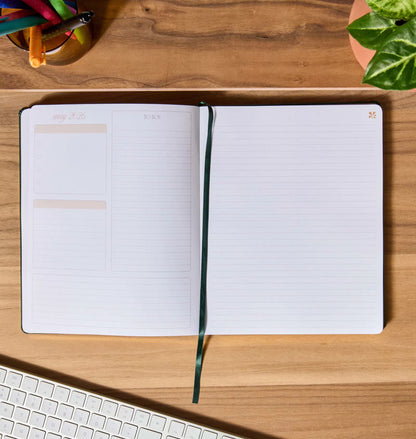 Open notebook on a wooden desk with a keyboard and colorful pens.