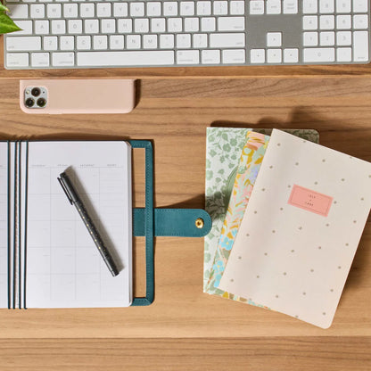 Desk setup with notebooks, pen, and keyboard on a wooden surface