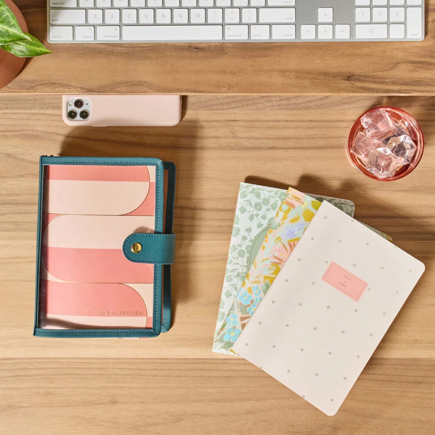 Desk with notebooks, a phone, and a keyboard on a wooden surface
