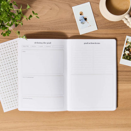Open planner on a wooden table with a cup of coffee and photos
